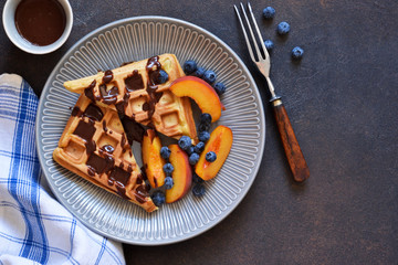 Vanilla Belgian waffles with chocolate sauce, peaches and berries in a plate on the kitchen table.