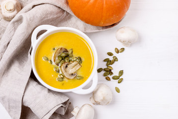 Bowl of Homemade Pumpkin and Mushrooms Soup with Cream and Pumpkin Seeds on Linen Napkin White Wooden Background Top View Copy Space