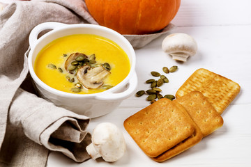 Bowl of Pumpkin and Mushrooms Soup with Cream and Pumpkin Seeds on Linen Napkin White Wooden Background Raw Mushrooms Pumpkin Seeds and Galette View from Above