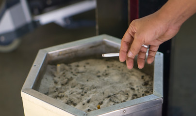 Man hands are holding a cigarette in a smoking area.