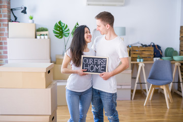 Fototapeta na wymiar Young beautiful couple standing on the floor holding blackboard with message at new home around cardboard boxes