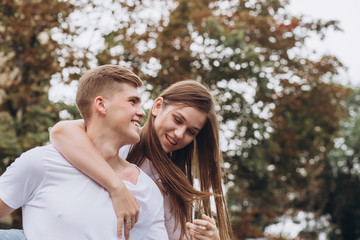 Fototapeta premium Happy young couple walks the streets of the city and hold hands. guy and girl in white t-shirts and jeans outdoors. Teenagers cuddling against the backdrop of an autumn tree. Couple close-up portrait
