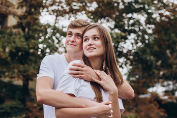 Fototapeta premium Happy young couple walks the streets of the city and hold hands. guy and girl in white t-shirts and jeans outdoors. Teenagers cuddling against the backdrop of an autumn tree. Couple close-up portrait