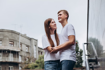 Happy young couple walks the streets of the city and hold hands. guy and girl in white t-shirts and jeans outdoors. Teenagers hug on the background of the urban landscape. Couple close up portrait.