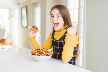 Beautiful young girl eating chocolate chips muffins screaming proud and celebrating victory and...