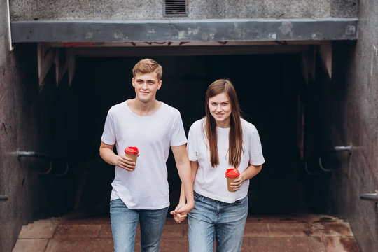 Molodaya para p'yet kofe iz kartonnykh chashek. Podrostki paren' i devushka podnimayutsya po stupen'kam na ulitsu. Muzhchina i zhenshchina v belykh futbolkakh i dzhinsakh v metro.