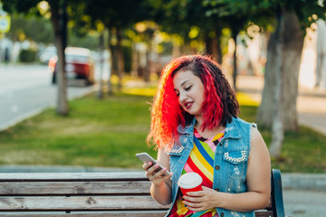 Stylish happy young woman in a bright striped sundress and a denim T-shirt with red hair walks along the street. Portrait of a smiling girl with a mobile phone