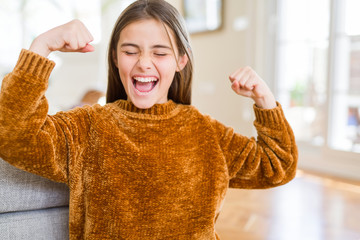 Beautiful young girl kid wearing casual sweater excited for success with arms raised celebrating victory smiling. Winner concept.