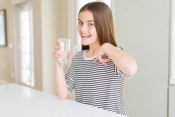 Beautiful young girl kid drinking a fresh glass of water with surprise face pointing finger to himself