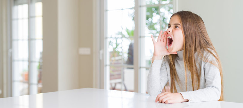 Wide angle picture of beautiful young girl kid wearing casual sweater shouting and screaming loud to side with hand on mouth. Communication concept.