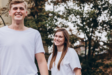 Fototapeta premium Happy young couple walks the streets of the city and hold hands. guy and girl in white t-shirts and jeans outdoors. Teenagers cuddling against the backdrop of an autumn tree. Couple close-up portrait