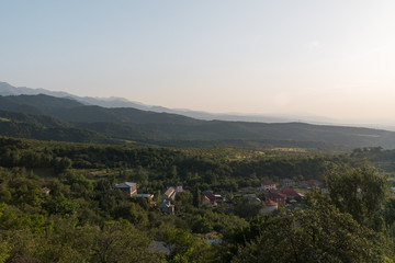 Summer in the mountains of Kazakhstan. Green fields and slopes, trees growing right on the mountains and the distant snowy peaks of the mountains. On the slopes visible houses of local residents.