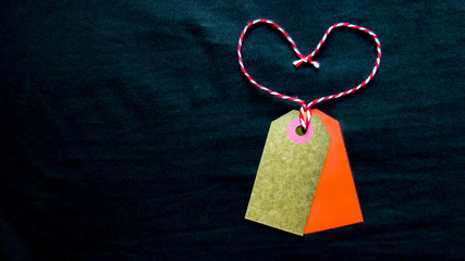 two cardboard tags and a red heart-shaped rope on a black background. Copy space, place for text, flat lay.