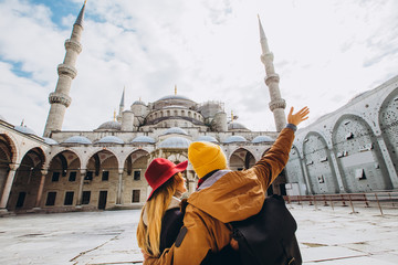 Naklejka premium Młoda para Europejczyków spaceruje po dziedzińcu Błękitnego Meczetu w Stambule w Turcji. Podróżnik i dziewczyna w żółtych kapeluszach chodzą zimą w Stambule pochmurny jesienny dzień w Stambule.