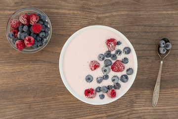 Yogurt smoothie with frozen raspberries, blueberries and coconut shavings over wooden background. Healthy food concept. Top view.