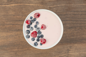Yogurt smoothie with frozen raspberries, blueberries and coconut shavings over wooden background. Healthy food concept. Top view.