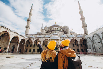 A young European couple walks in the courtyard of the Blue Mosque in Istanbul, Turkey. Traveler guy and girl in yellow hats walk in winter Istanbul. cloudy autumn day in Istanbul.