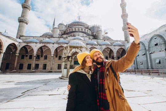 A young European couple walks in the courtyard of the Blue Mosque and takes a selfie, Istanbul Turkey. Traveler guy and girl in yellow hats are photographed in winter Istanbul.