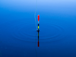 A fishing float floats on the water of the lake making circles in the water. © Andrey