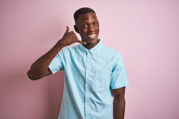 African american man wearing blue casual shirt standing over isolated pink background smiling doing phone gesture with hand and fingers like talking on the telephone. Communicating concepts.