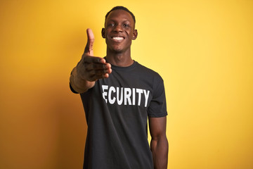 African american safeguard man wearing security uniform over isolated yellow background smiling friendly offering handshake as greeting and welcoming. Successful business.