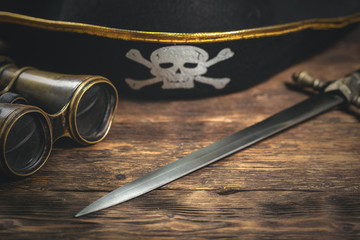 Pirate hat, binoculars and a dagger on a brown wooden table background.