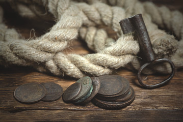 Old coins, rope and key from treasure chest on a wooden table background.