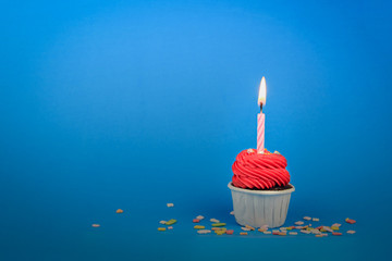 Sweet red cupcake with bow candle on blue background with copy space. Happy birthday party concept background.