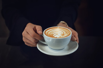 Closeup of girl hands holding white cup of latte art coffee with dark background