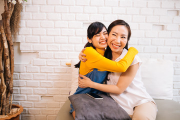 Loving smiling Asian women hugging happily while sitting together on couch at living room