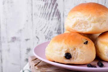 Yeast buns with raisins on ceramic plate on white wooden table