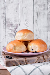 Yeast buns with raisins on ceramic plate on white wooden table