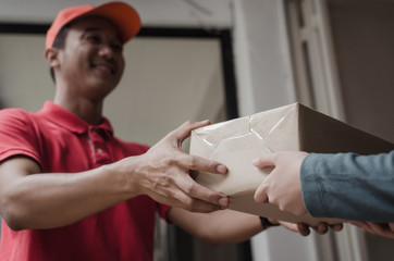 young delivery service man in red uniform smiling with woman customer receiving parcel post box from courier at home, cargo shipping, express delivery service, online shopping and logistics concept