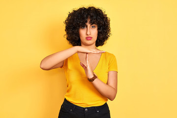 Young arab woman with curly hair wearing t-shirt standing over isolated yellow background Doing...