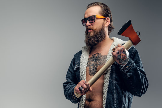 Brutal bearded man in sunglasses and denim jacket is holding axe.