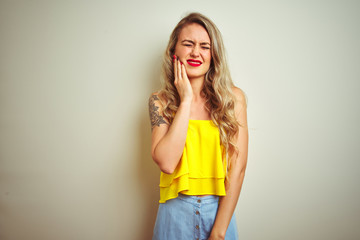 Young beautiful woman wearing yellow t-shirt standing over white isolated background touching mouth with hand with painful expression because of toothache or dental illness on teeth. Dentist concept.