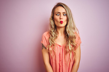 Young beautiful woman wearing t-shirt standing over pink isolated background making fish face with lips, crazy and comical gesture. Funny expression.