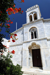 Fototapeta na wymiar Red Campsis grandiflora flowers leading to Marble front of 13th century Roman catholic cathedral inside the Chora’s Castle (Kastro), Naxos, Greek Islands