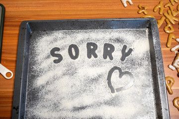 the word Sorry is written on a baking tray sprinkled with icing sugar or flour
