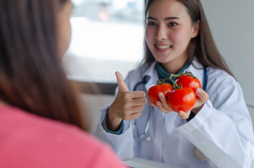 Nutritional. friendly nutritionist female doctor medical showing thumbs up with fresh red tomato and vegetable to young patient in office hospital, nutrition, diet, food science, healthy food concept