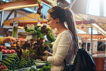 Young attractive woman with tattooes is choosing fresh salad at vegetable market.