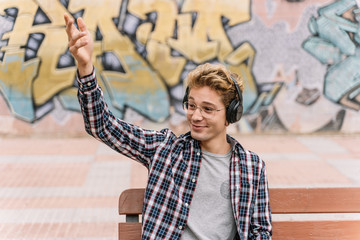 Obraz premium young man listening to music is waving hand and sitting on a bench