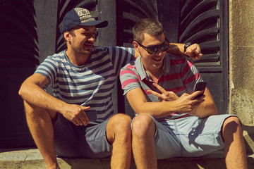 Male friends using cellphone outdoors.