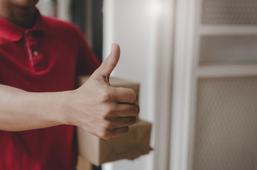 delivery service man in red uniform showing thumbs up and holding receiving parcel post box ready send to customer at home, cargo shipping, express delivery service, online shopping, logistics concept
