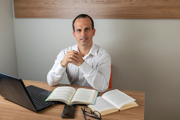 43 year old Man, next to his books, looking at the camera and smiling.