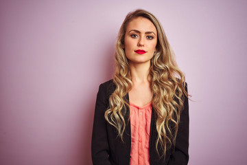 Young beautiful business woman wearing elegant jacket standing over pink isolated background with serious expression on face. Simple and natural looking at the camera.