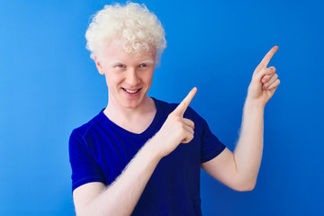 Young albino blond man wearing casual t-shirt standing over isolated blue background smiling and...