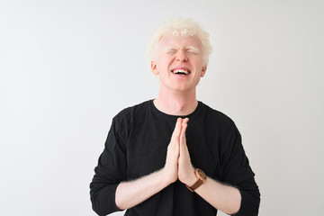 Young albino blond man wearing black t-shirt standing over isolated white background begging and praying with hands together with hope expression on face very emotional and worried. 