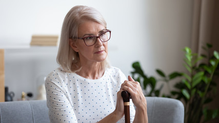 Upset mature woman holding wooden cane, thinking about future