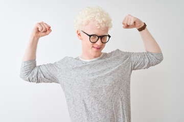 Young albino blond man wearing striped t-shirt and glasses over isolated white background showing arms muscles smiling proud. Fitness concept.